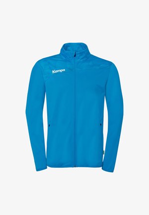 Veste bleue à fermeture éclair intégrale avec col montant, motif géométrique subtil sur la poitrine, deux poches latérales zippées et logo "Kempa" blanc sur la poitrine gauche.