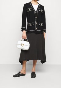 Černý kardigan se zlatými knoflíky a dekorativním lemem; rozšířená černá sukně; bílá prošívaná kabelka se zlatými prvky; černé slip-on boty.