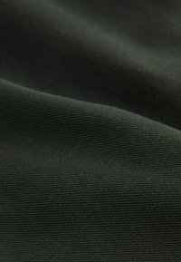 Dark green textured fabric with a ribbed pattern, soft to the touch. The surface shows fine fibers and subtle variations in shading.