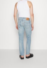 Ljusblå denimjeans med slim fit, synlig sömnad och en beige läderlapp på baksidan av midjan. Matchas med svarta platåsandaler.