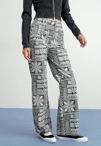 Black and white patterned flared pants with geometric designs; fabric appears smooth with a slight sheen. Worn with a dark cropped top and black sneakers.