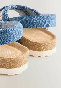 Sandali in stile denim con cinturini in tessuto blu, una soletta testurizzata color tan e una suola simile al sughero con bordo bianco.