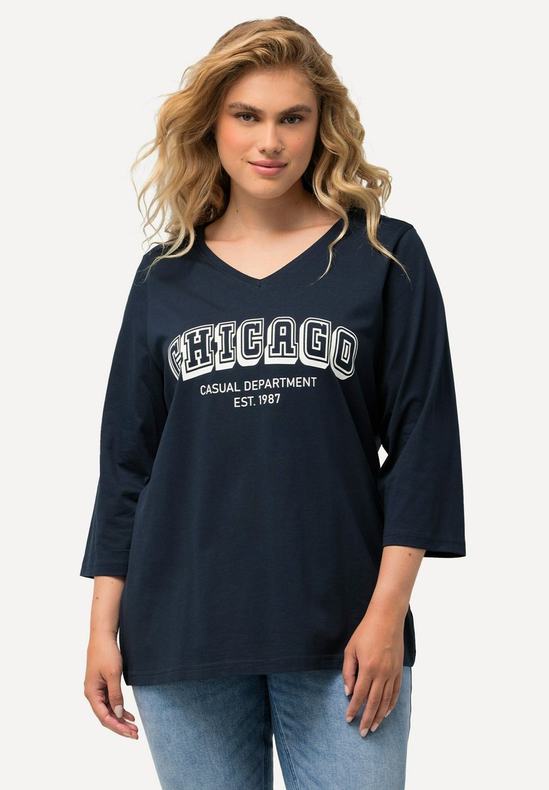 Marineblaues V-Ausschnitt-Shirt mit drei Viertel-Ärmeln, auf dem in fetten weißen Buchstaben "CHICAGO CASUAL DEPARTMENT EST. 1987" gedruckt ist.