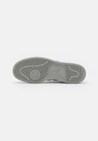 Szara i biała podeszwa sneakersów New Balance, ukazująca wzory bieżnika oraz logo marki na jednolitym białym tle.