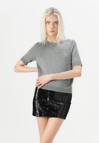 Gray knitted sweater with short sleeves, embellished with small white pearls, paired with a black sequined mini skirt.