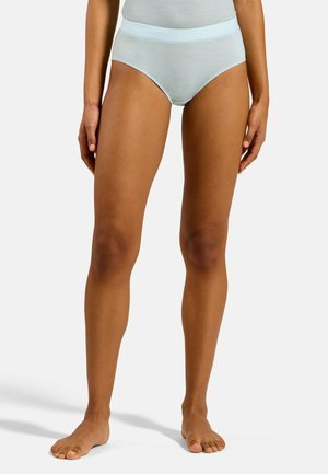 Femme portant des sous-vêtements bleu clair, debout pieds nus sur un fond blanc uni, montrant le devant et les jambes.