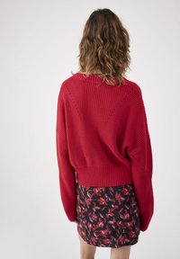 Czerwony sweter dziergany z szerokim, prążkowanym dołem i ukośnymi szwami, w połączeniu z dopasowaną spódnicą w kwiatowy wzór.