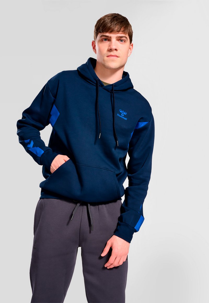 Sweat à capuche bleu marine avec des accents bleus contrastants, capuche à cordon de serrage et poche avant. Associé à un pantalon de survêtement gris avec une taille élastique.