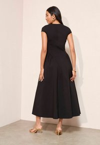 Musta põlveni ulatuv kleit lühikeste küljega varrukatega, istuv bodi ja kogutud seelikuga. Omab siledat tekstuuri ja peeneid õmbluste detaile.