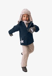Manteau d'hiver bleu marine avec capuche à fourrure, pantalons beiges, gants gris et un accent en étoile blanche sur la poche du manteau.