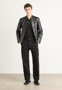 Black leather jacket with a stand collar, paired with a fitted black shirt and straight-leg black pants. Completing the look are black shoes.