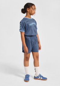 Blaues Sportoutfit mit einem kurzärmligen Shirt mit horizontalen Streifen, passenden Shorts und blauen Turnschuhen mit weißen Akzenten.