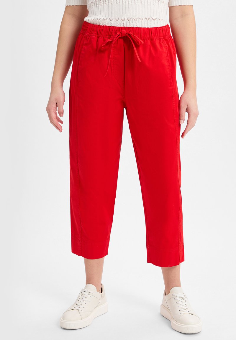 Red cropped pants with a soft texture, featuring an elastic waistband and drawstring. Paired with white sneakers for a casual look.
