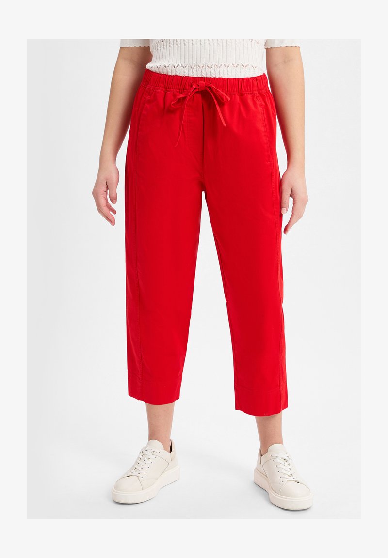 Red cropped pants with a soft texture, featuring an elastic waistband and drawstring. Paired with white sneakers for a casual look.