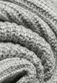 Šedá pletená deka s texturovaným vzorem, složená do spirály. Tkanina vypadá měkce a hustě, s viditelnými vlákny a robustním pleteným designem.