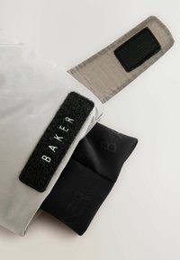 Grå tekstilpose med en sort Velcro-strop, som har ordet "BAKER" prægede i sort på fronten og et sort bundstykke.