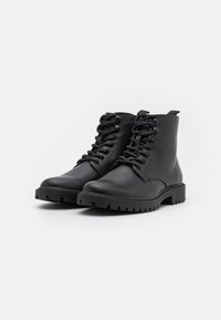 Botas de tobillo de cuero negro con diseño de cordones, suela de goma resistente y acentos de costura; cuentan con tiradores para ponerse fácilmente.
