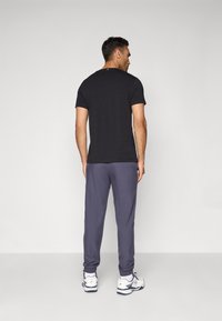 Zwarte t-shirt met korte mouwen, gecombineerd met grijze joggingbroeken. Witte sportschoenen zichtbaar, met blauwe en rode accenten. Eenvoudig ontwerp, zachte textuur.