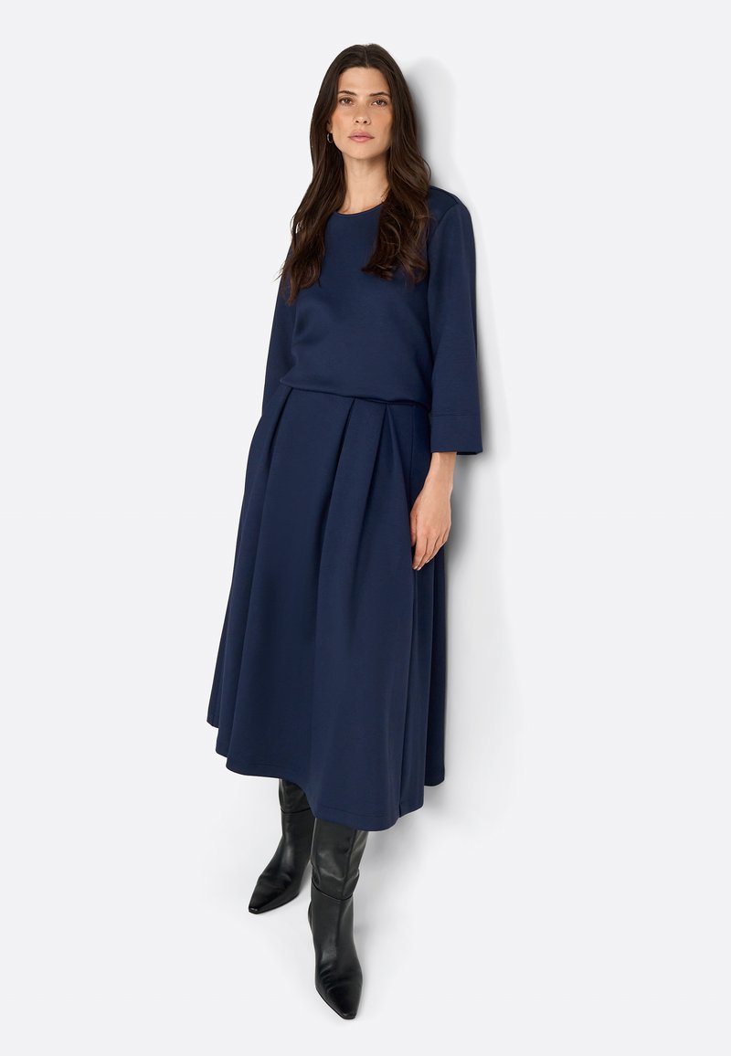 Navy blue kaksiosainen asu, johon kuuluu pitkähihaista puseroa ja ryhmäkäärmeitä, joita korostavat polven ylle ulottuvat mustat korkokengät. Sileä pinta.