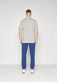Gray heathered polo shirt with a relaxed fit, paired with blue trousers, and white sneakers, viewed from the back.