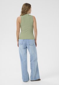 Tajta ärm-lös olivgrön topp med en texturerad yta, i kombination med ljusblå vida jeans med bakfickor och sömdetaljer.