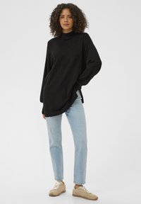 Pulover negru cu mâneci lungi, guler înalt și croială largă, asortat cu blugi drepti albastru deschis și adidași bej.