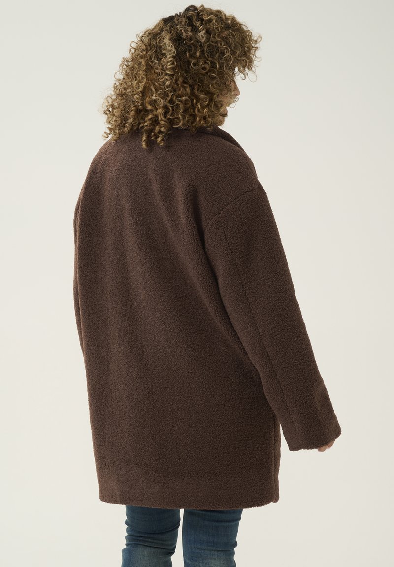 Brauner oversized Fleece-Mantel mit lockerer Passform, abgerundeten Schulternähten und langen Ärmeln, der eine weiche, strukturierte Oberfläche aufweist.