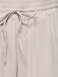 Pantalon en tissu beige avec ceinture élastique et cordon noué au centre devant, montrant la texture et les détails de la couture.