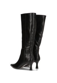 Botas de cuero negras hasta la rodilla con punteras afiladas y tacones de kitten curvados, mostradas desde un ángulo trasero a tres cuartos sobre fondo blanco.