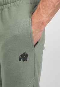 Groene katoenen joggers met een zwart gorilla-logo bedrukt op de onderkant van de linkerzak, met een zijzak en een gestructureerde stof.