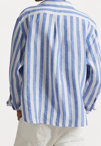Blå och vit randig linneskjorta med en bakfåll, avslappnad passform och knäppte ärmar. Mjuk textur med en lätt känsla.
