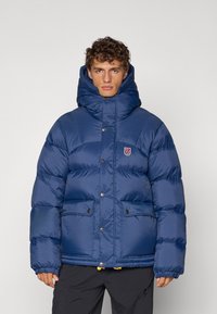 Navy blue puffer jacket with a high collar, snap buttons, and two front pockets. Smooth texture with padded sections for insulation.
