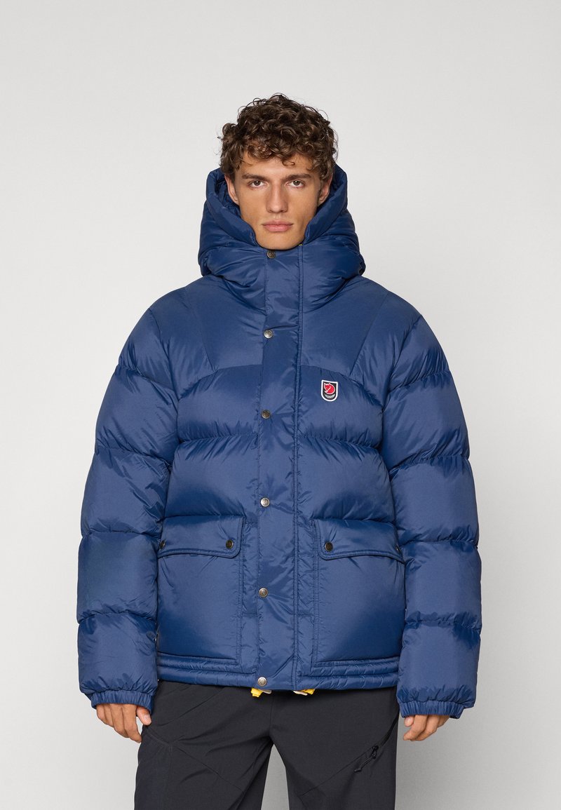 Navy blue puffer jacket with a high collar, snap buttons, and two front pockets. Smooth texture with padded sections for insulation.