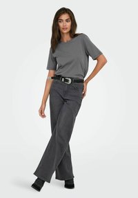 Camiseta de algodón gris con mangas cortas, combinada con jeans de pierna ancha gris oscuro. Cinturón negro con hebilla plateada como acento. Diseño simple y moderno.