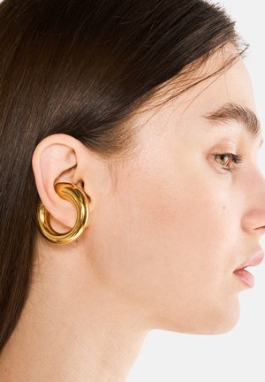 Boucle d'oreille en or avec un design torsadé, une texture lisse et une forme audacieuse, portée sur l'oreille externe avec une coiffure élégante.