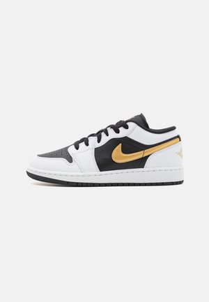 Niskie sneakersy w kolorach czarnym, białym i złotym, z czarnymi sznurowadłami, perforowanym przodem i złotym logo Nike po bokach.