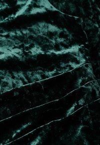 Tissu en velours vert foncé avec une texture douce, présentant un motif ondulé et des plis, créant profondeur et dimension dans le matériau.