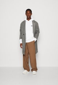 Cappotto grigio in misto lana sopra una felpa bianca, abbinato a pantaloni larghi beige e sneakers bianche. Il cappotto presenta un design doppiopetto.