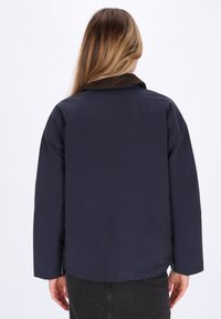 Mørkeblå jakke med en kordfløjlskrage, afslappet pasform og lange ærmer. Glat tekstur, med et enkelt design og minimal dekoration.