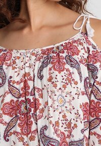Blouse scollata in bianco con motivi paisley e floreali colorati. Presenta spalline regolabili e un tessuto testurizzato.