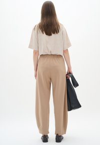 Beige oversized t-shirt, högmidjade beige byxor och svart läderväska. Slätt tyg och avslappnad passform med elastisk midja.
