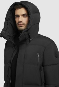 Giacca a vento nera con grande cappuccio, caratterizzata da una tasca con zip sul lato sinistro del petto e una texture imbottita. Design semplice e funzionale.