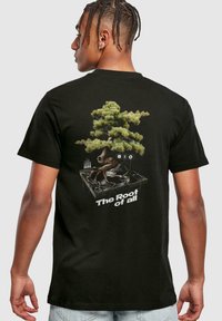 Černé bavlněné tričko s grafickým designem bonsai stromu a gramofonu, s nápisem "Kořen všeho" v bílé barvě.