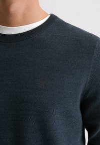 Granatowy, ciemny sweter dziany, z okrągłym dekoltem i teksturowanej tkaniny, z subtelnym logo na środku, z prążkowanymi mankietami i ściągaczem.