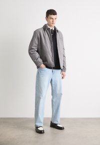 Grå kordfløjljakke med elastiske manchetter, båret over en sort polo-skjorte, parret med lyseblå lige ben-joggingbukser og sorte loafers med hvide accenter.