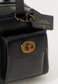 Crna kožna torba s pozlaćenim okretno kopčom, zatvaranjem na zip, i oznakom na kojoj piše "The Twin Turnlock Bag Limited Re-Edition 1968."