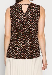 Top negro sin mangas con manchas abstractas multicolores y un pequeño corte en forma de lágrima en la parte superior de la espalda, combinado con una falda blanca con pliegues.