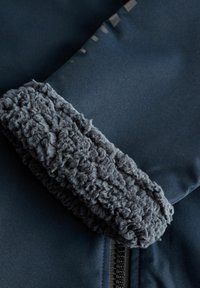Granatowa kurtka z miękką, teksturowaną, ciemnoszarym futrem na kołnierzu i mankietach, z gładkiego materiału z detalami na zamku.