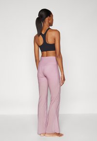 Must must spordirinnahoidja risti seljaga, millele on lisatud heleroosad laienevad joogapüksid, mis on sileda tekstuuri ja õmbluste detailidega.