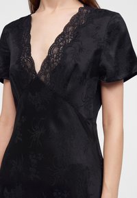 Robe en satin noire avec motif jacquard floral et décolleté en V profond bordé de dentelle, manches courtes, portée par une personne des épaules à la taille.